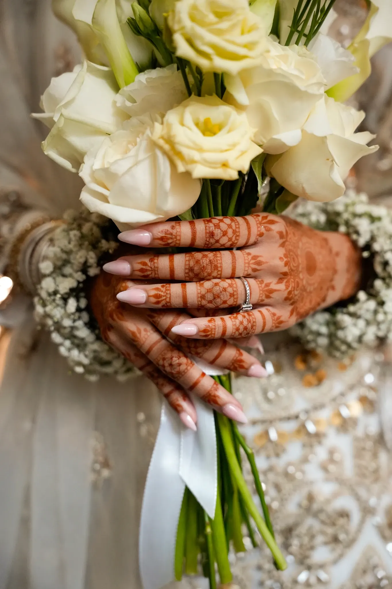 The bride's henna-painted hands hold a bouquet of white roses, with her ring and baby's breath at the wrists