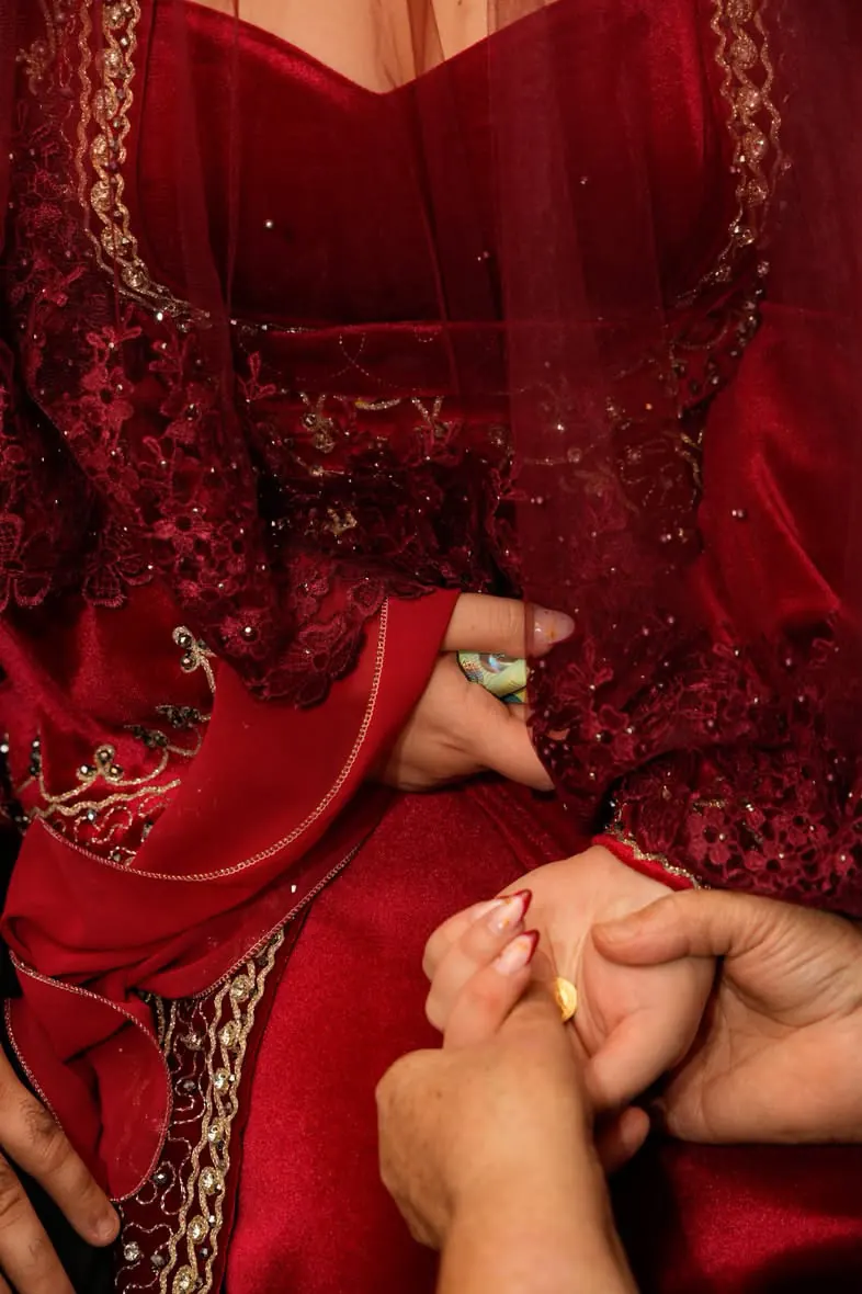 Eine ältere Hand hält die Hand der Braut im roten, goldbestickten Kleid, an ihrem Finger ein Ring