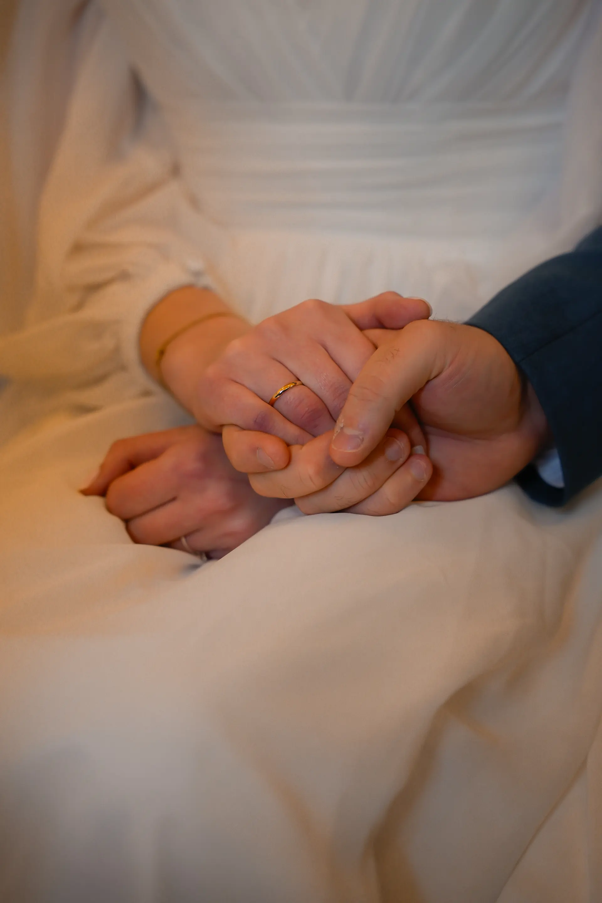 The couple's hands rest together on the bride's white dress, her wedding ring on her finger
